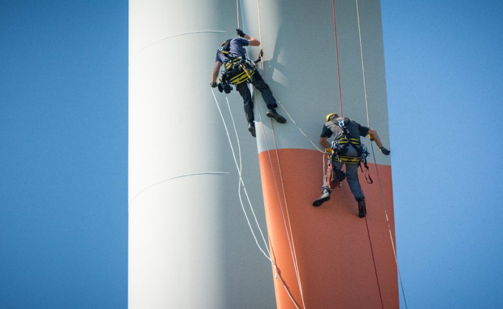 Engineers abseiling down a rotor blade of a wind turbine on a clear day with blue sky.