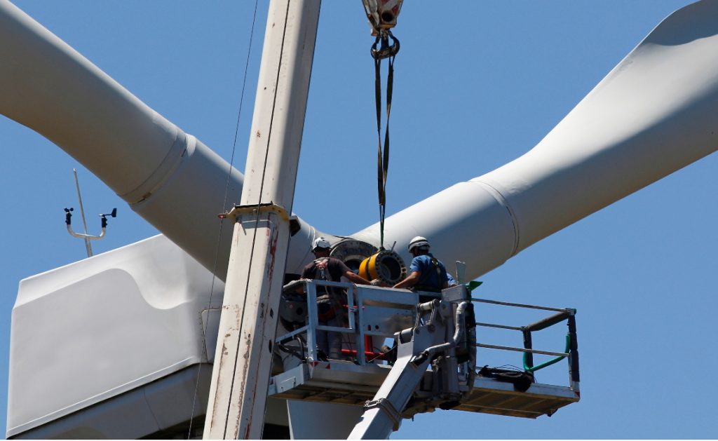 Wind turbine being repaired by engineers assisted by crane and elevator.